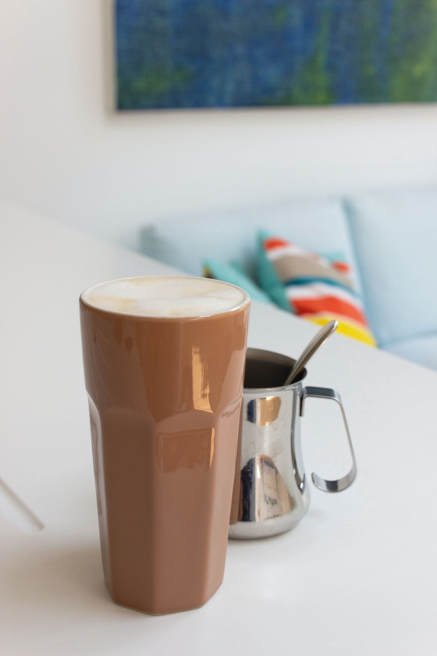 bruine lange mok met koffie en zilveren kan in woonkamer