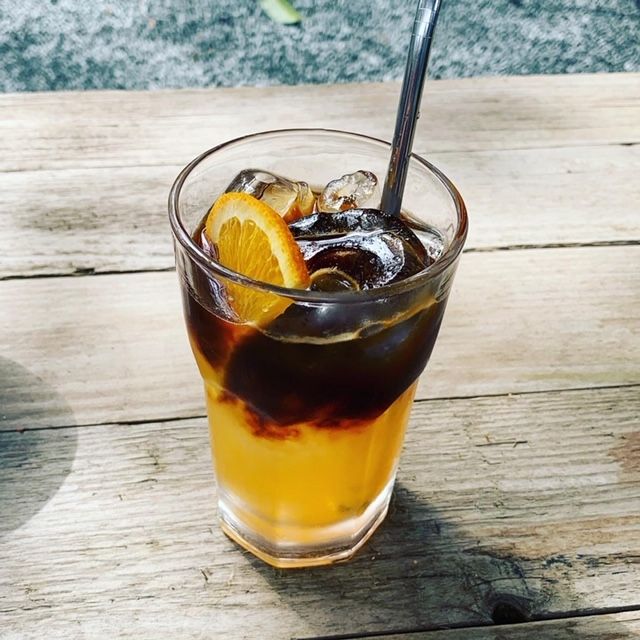 een glas orange koffie espresso met vers sinaasappelsap ijsklontjes en stalen rietje