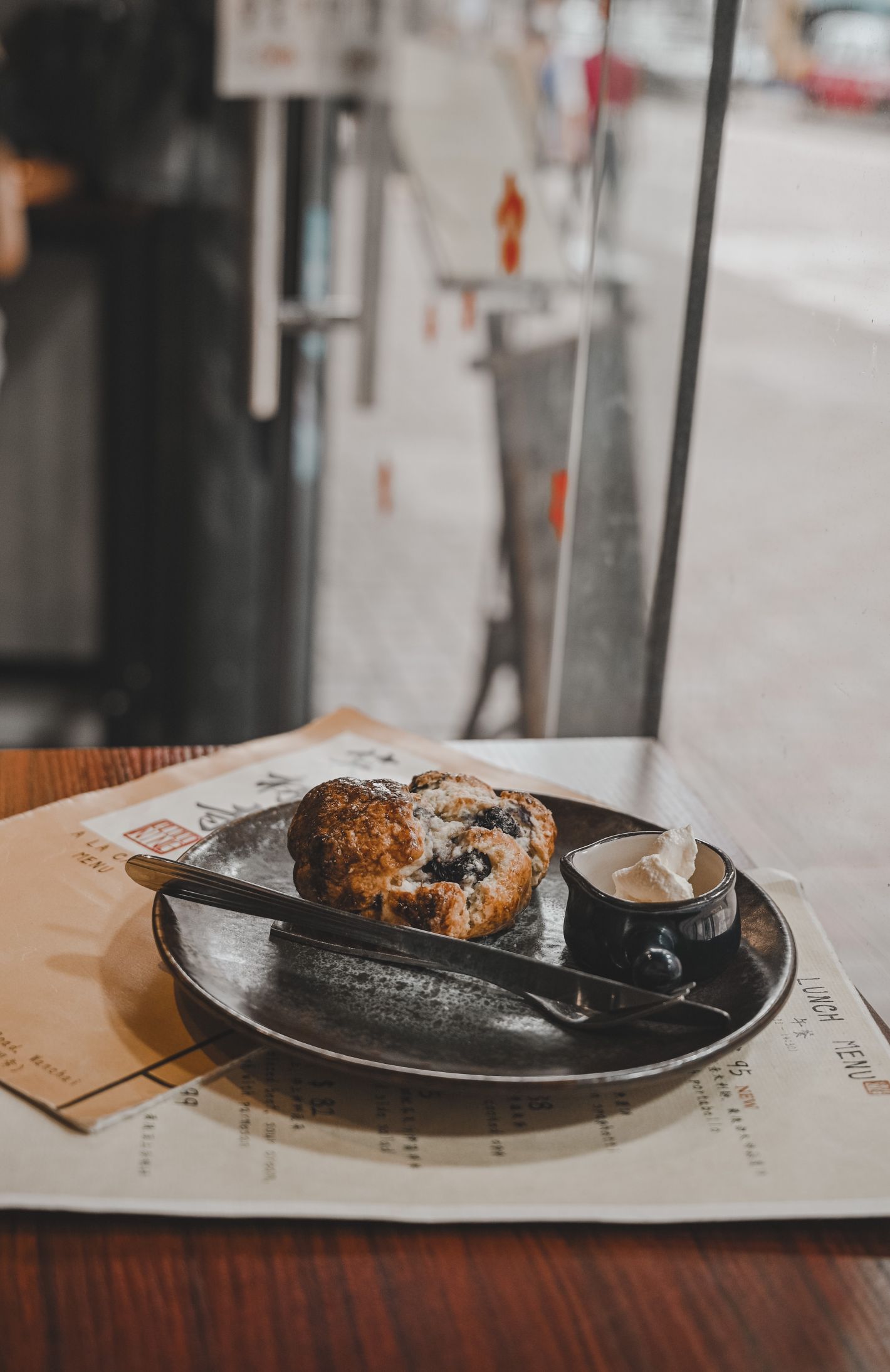 Een scone met rozijnen en room geserveerd op een zwart bordje bovenop een tafeltje met menukaart