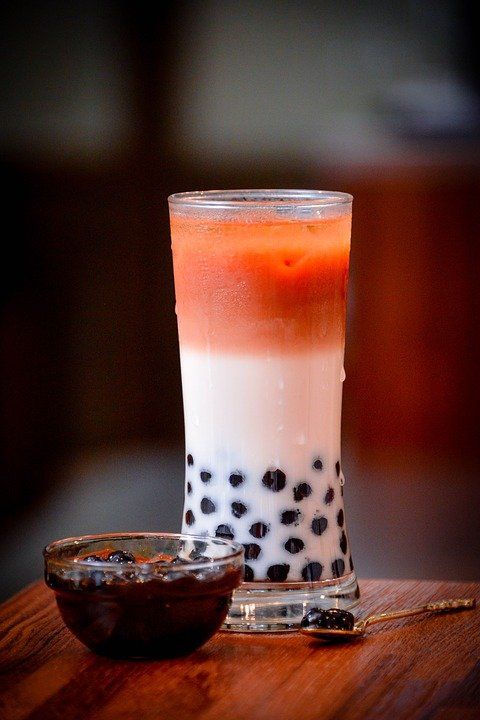 bubble tea drankje in longdrink glas met zwarte tapioca balletjes op de bodem. Drankje is wit op de bodem en in het midden rood bovenin.
