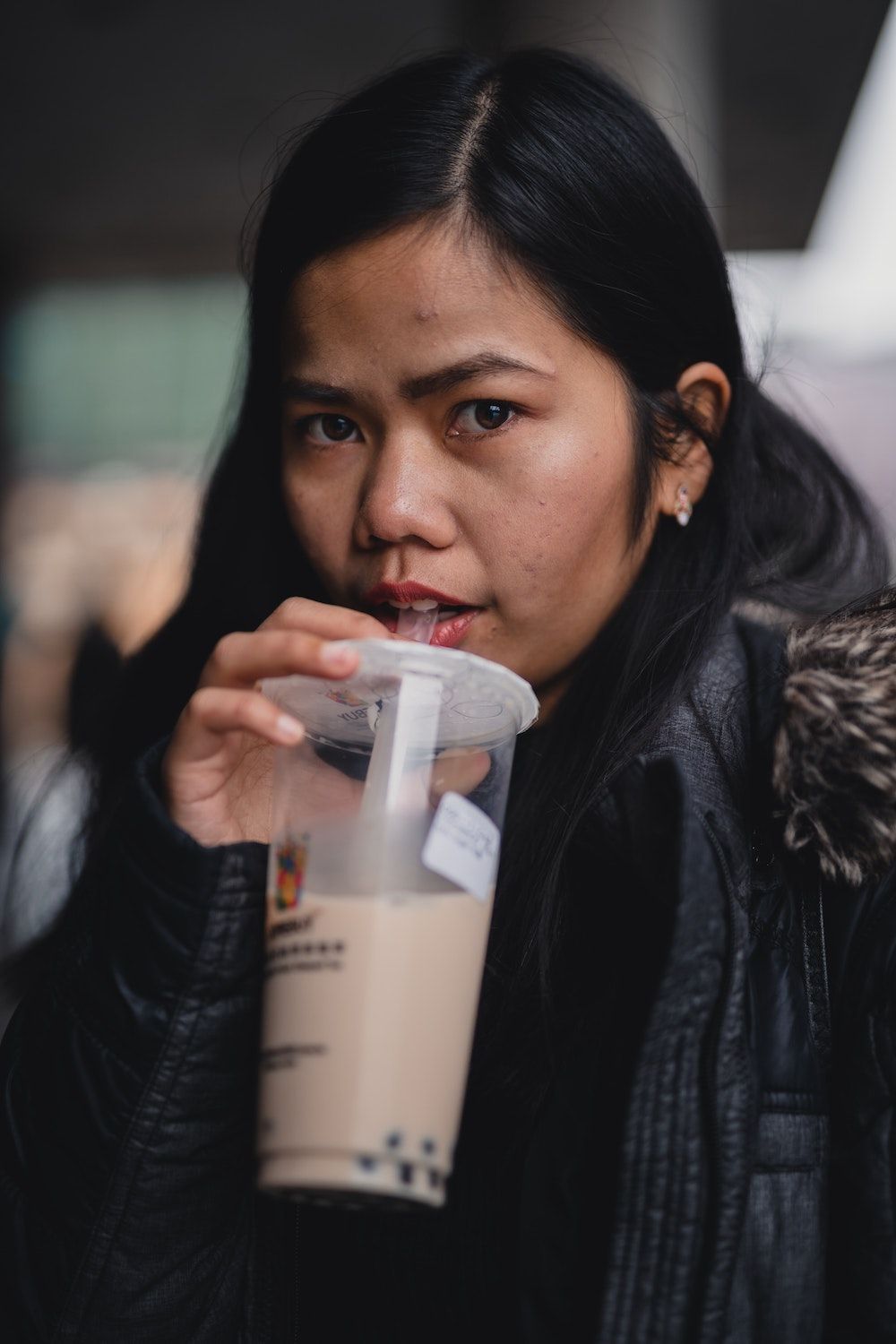 Vrouw uit Azië met lang zwart haar en winterjas met bontkraag die een bubbletea drinkt in plastic beker