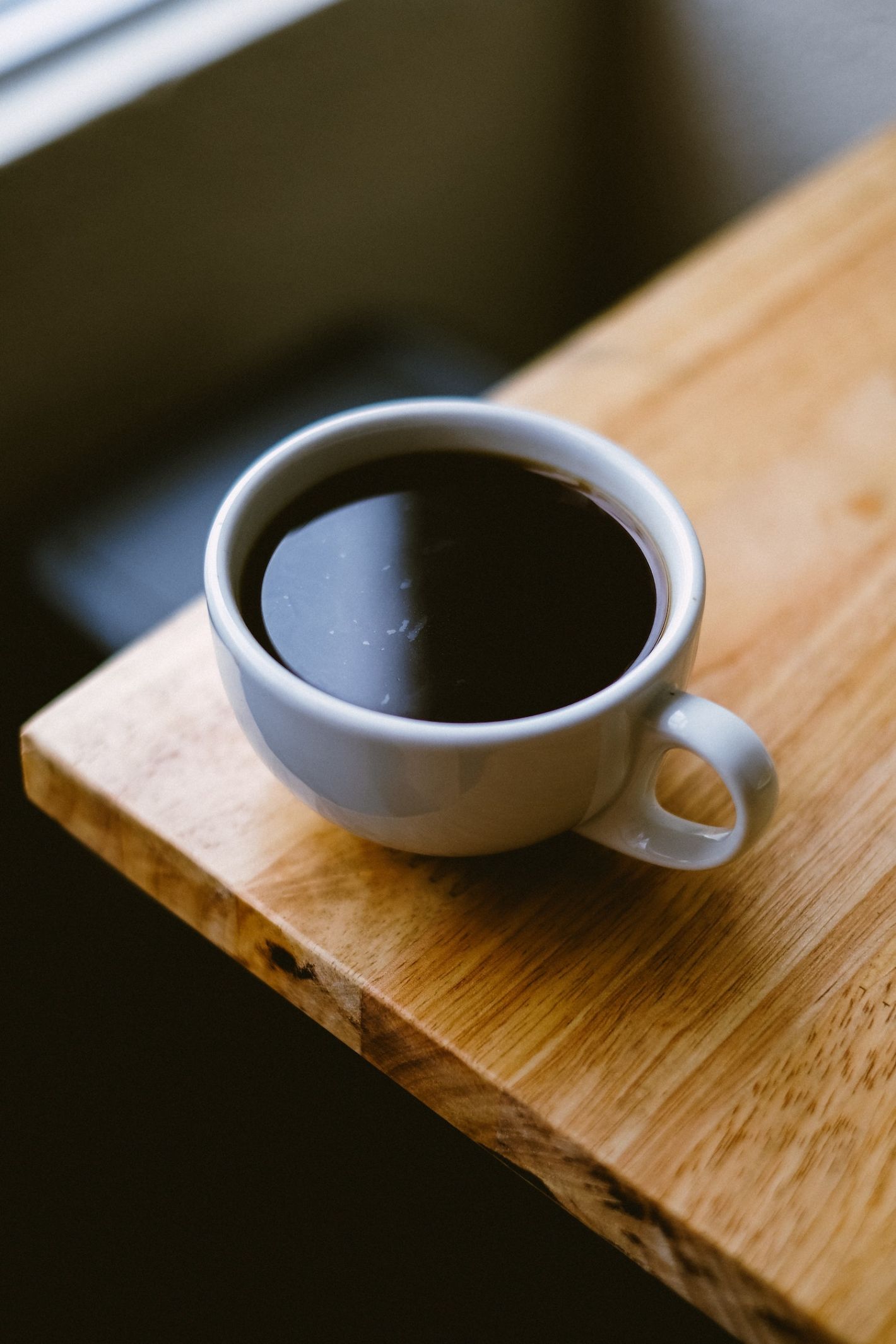 zwarte koffie in wit kopje op de hoek van een tafel