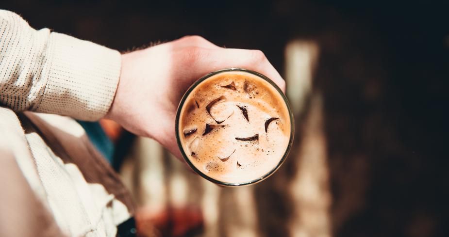 van bovenaf gefotografeerd persoon alleen bovenlichaam zichtbaar die een glas ijskoffie vasthoudt