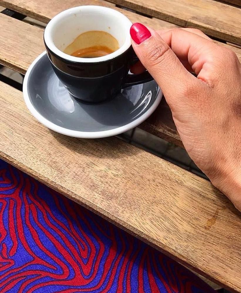 espresso in zwart kopje met schoteltje vast gehouden met een hand op een houten tuintje