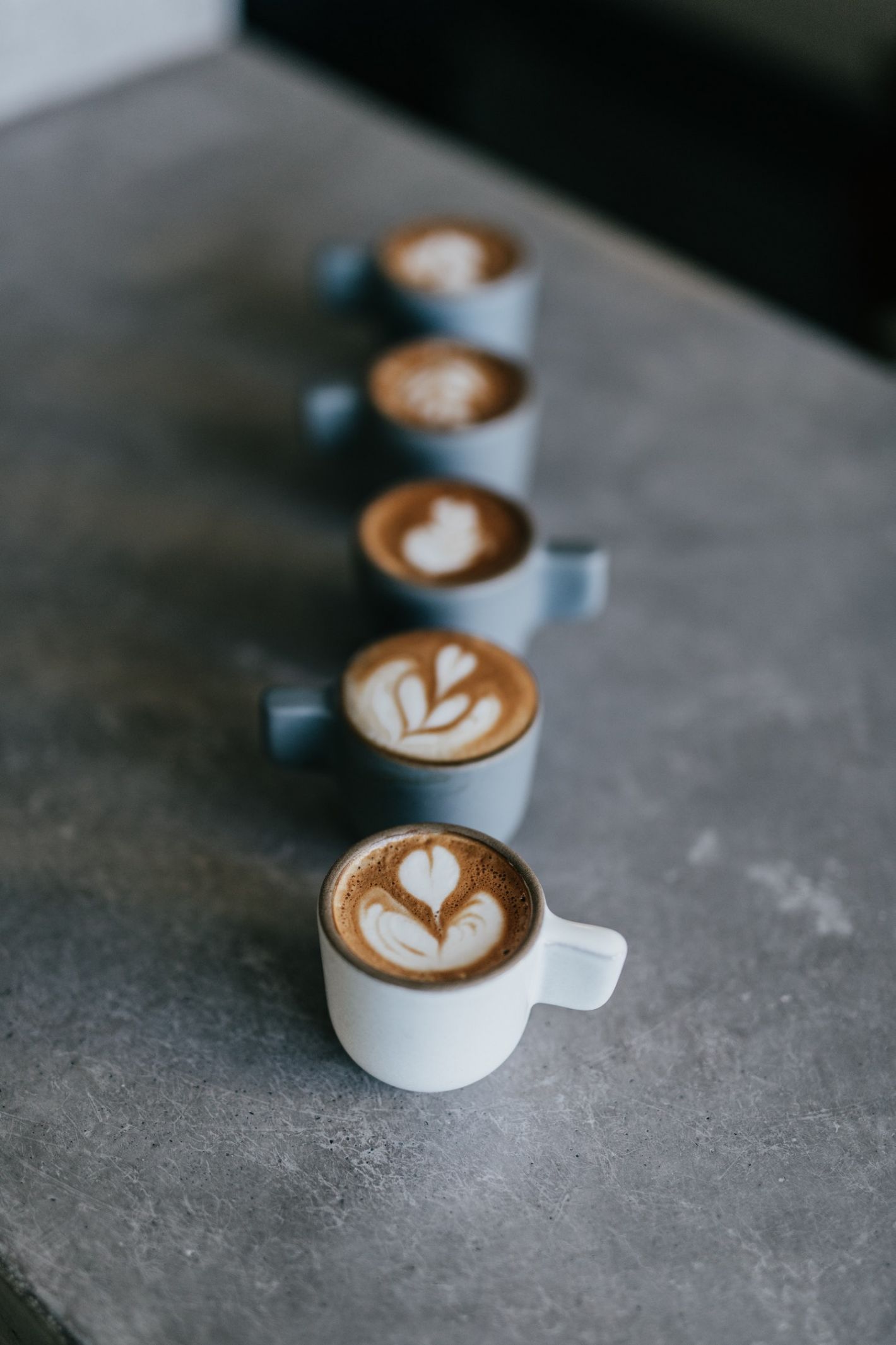 vijf kopjes cappuccino horizontaal op een rij op betonnen tafel