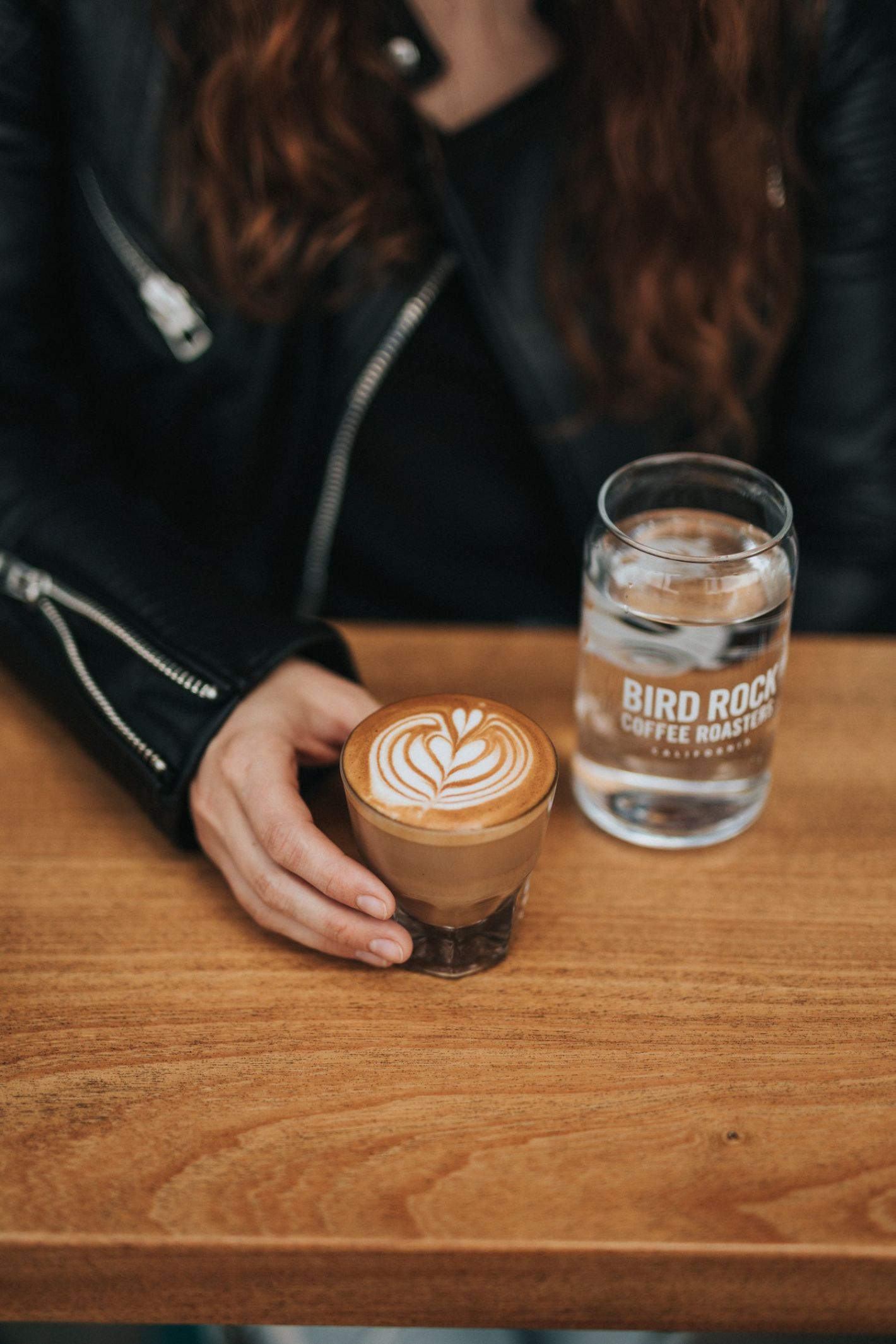 dame met leren jas houdt latte vast en glas water op de tafel