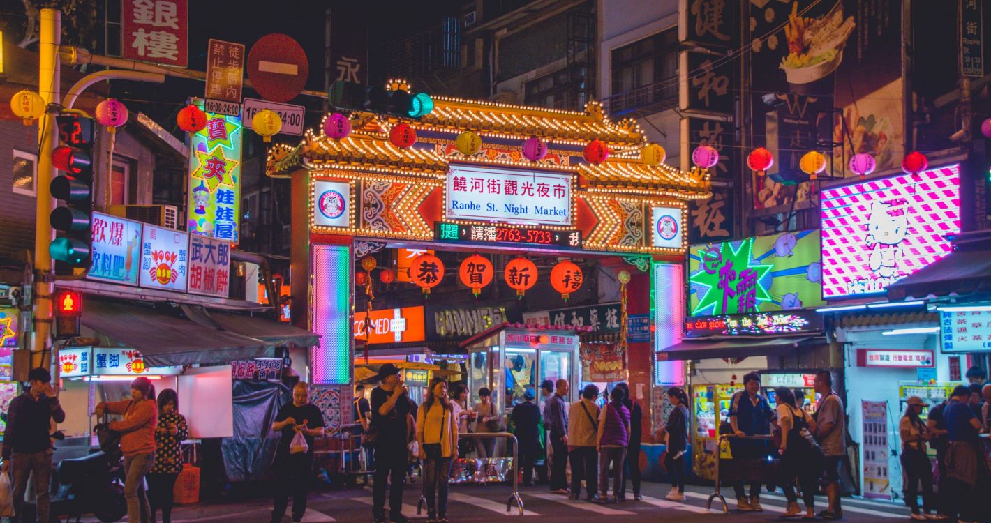 Zo'n 20 mensen die 's avonds een zebrapad oversteken in een stad in Taiwan met veel verlichting en neon borden