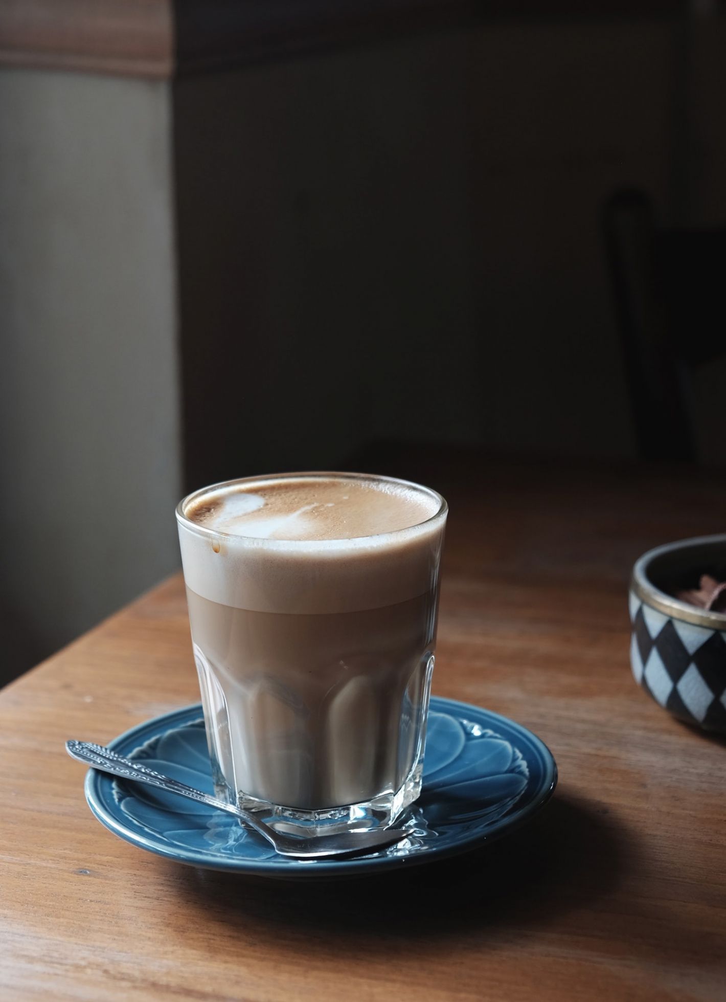 glas koffie met opgeschuimde melk op blauw schoteltje