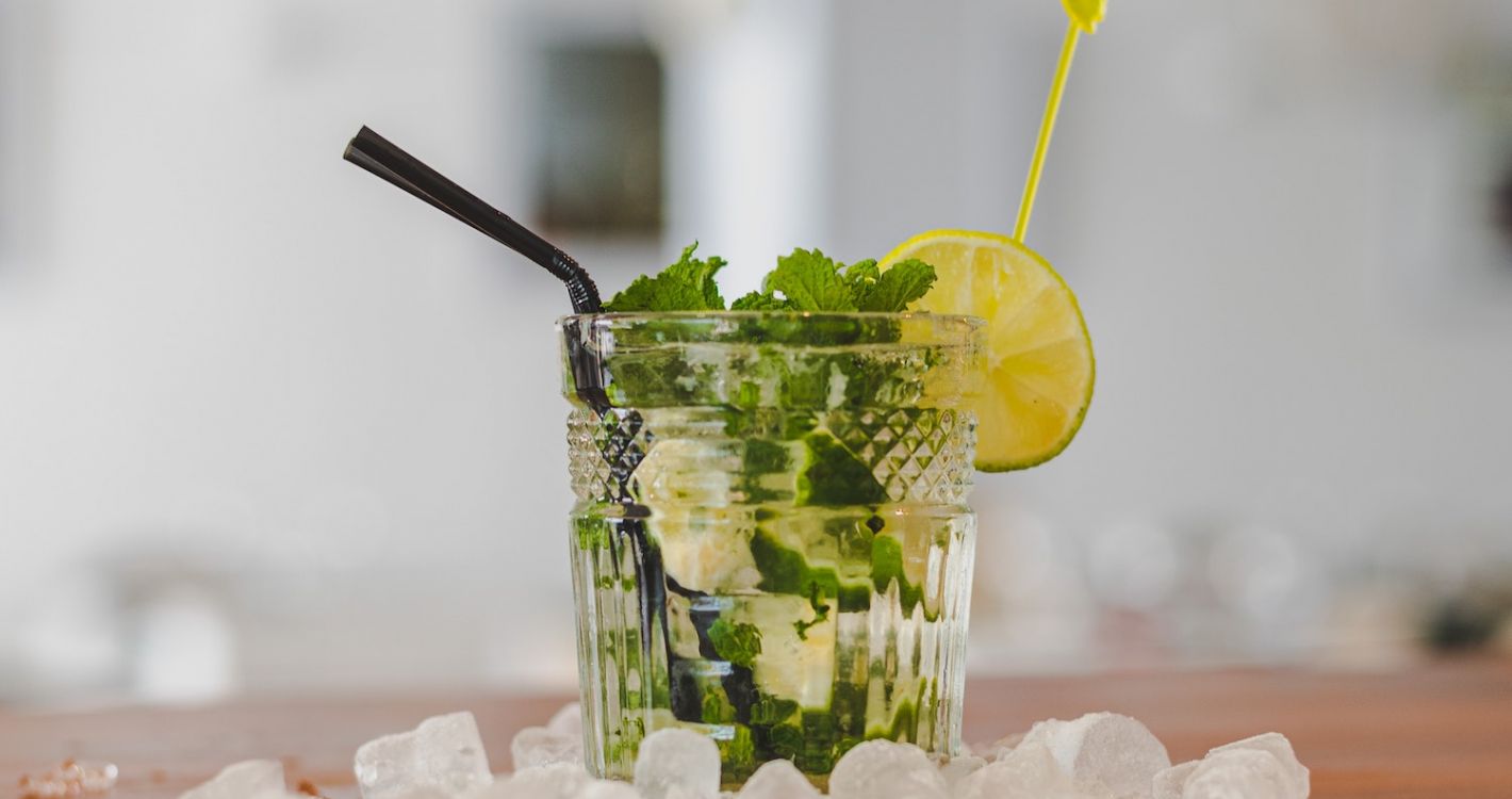 mojito cocktail met ijsklontjes en zwart rietje op houten tafel