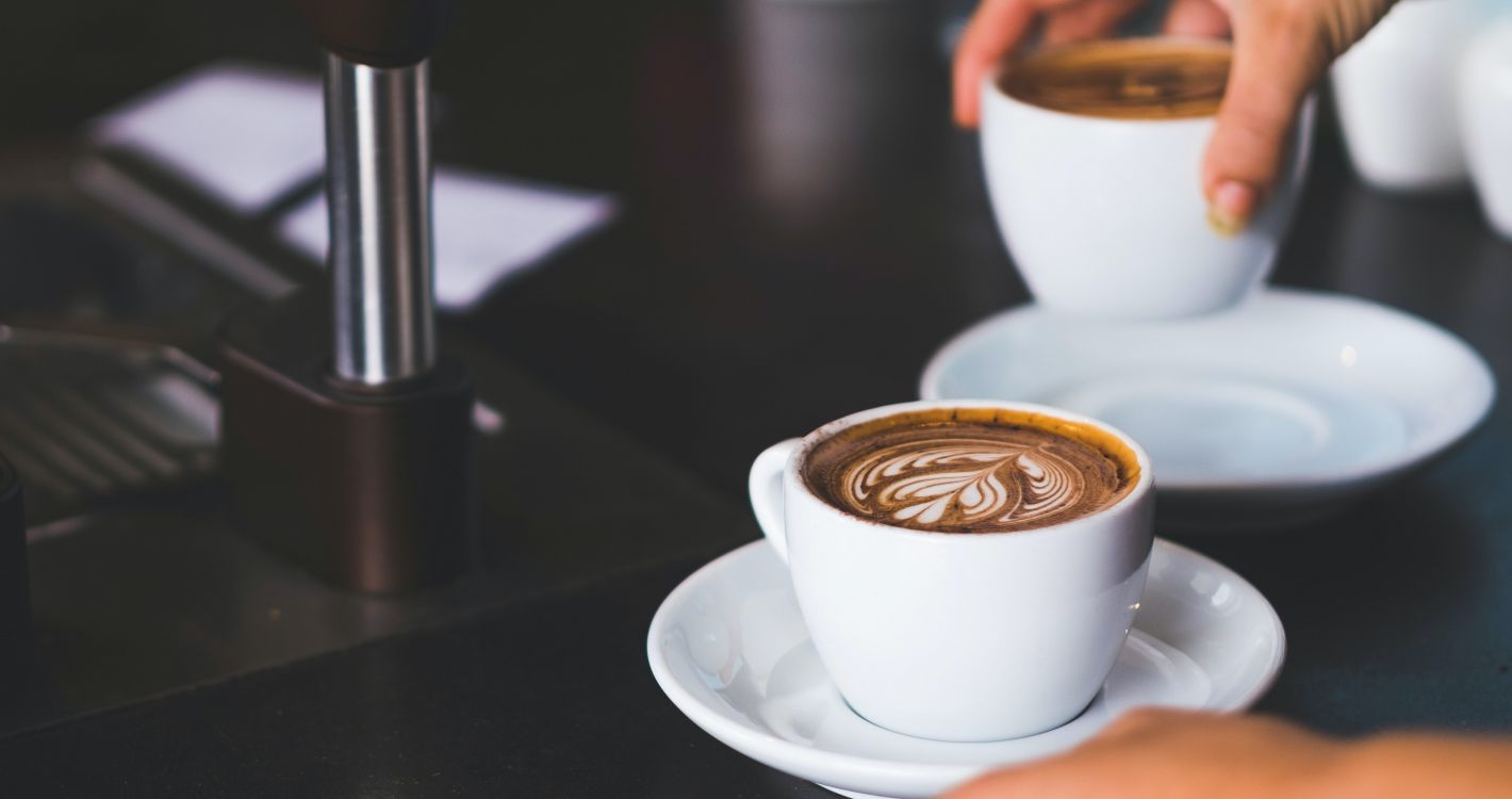 twee handen die twee witte kopjes cappuccino met latte art vasthouden