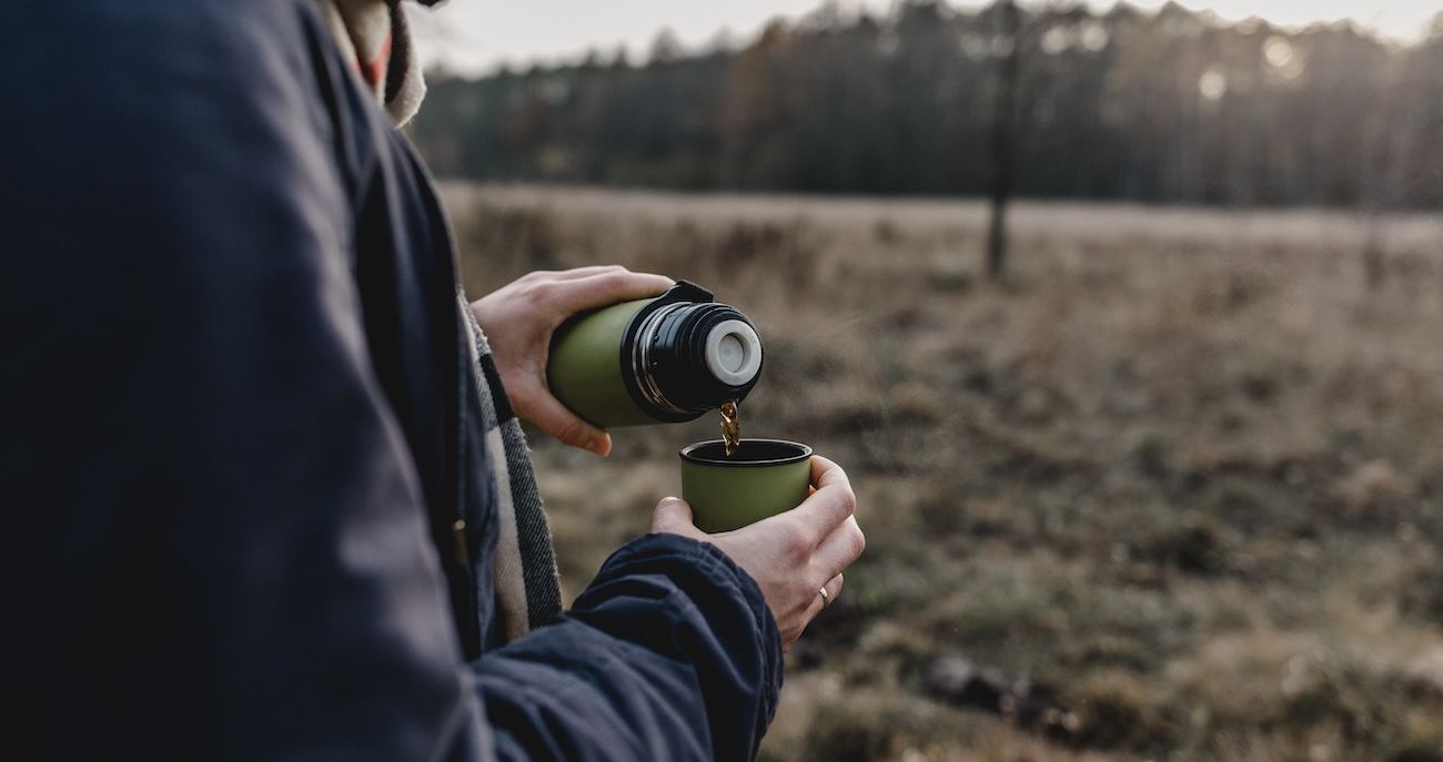 persoon die winterjas draagt een thermoskan met thee inschenkt en buiten in de natuur is