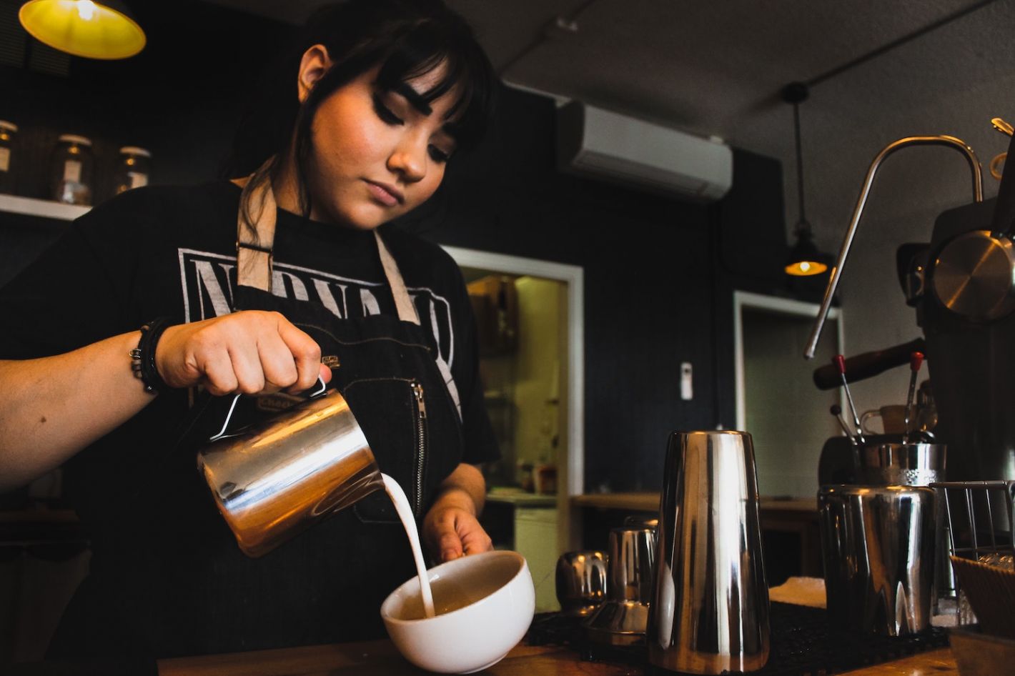 dame schenkt melk in koffiekopje in koffiezaak