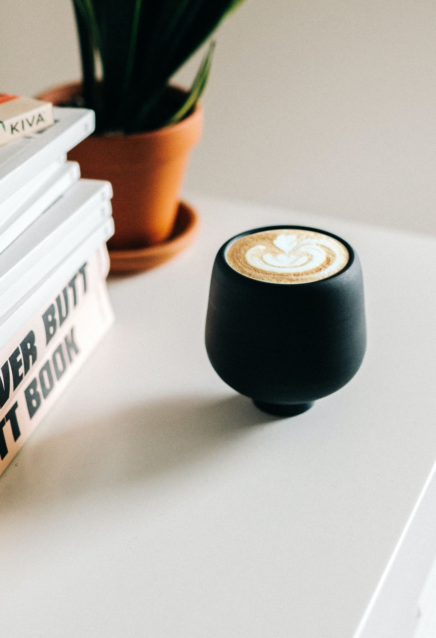 cappuccino zwart kopje op witte tafel met boeken en plantje op de achtergrond